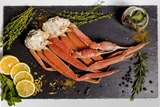A cluster of snow crab legs along with lemon slices and herbs on a slate serving board. thumbnail