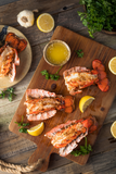 Cooked and split lobster tails with lemon wedges, fresh parsley and drawn butter on cutting board thumbnail