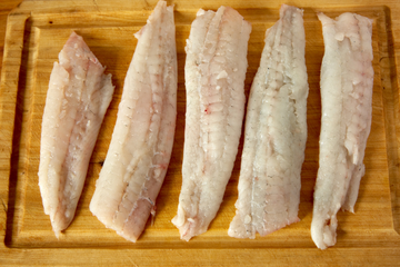 Several cleaned flounder fillets arranged on a wooden cutting board. 