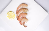 Four headless shrimp with lemon on top of white plate thumbnail