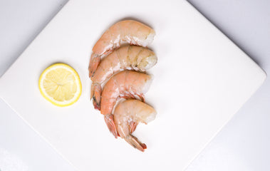 Four headless shrimp with lemon on top of white plate 