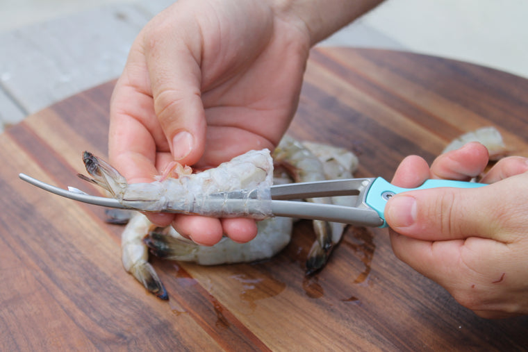 Hands using a Shrimp deveiner that is cleaning headless shrimp