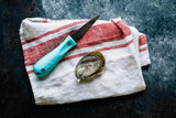 Oyster shucking knife next to oyster on top of tea towel thumbnail