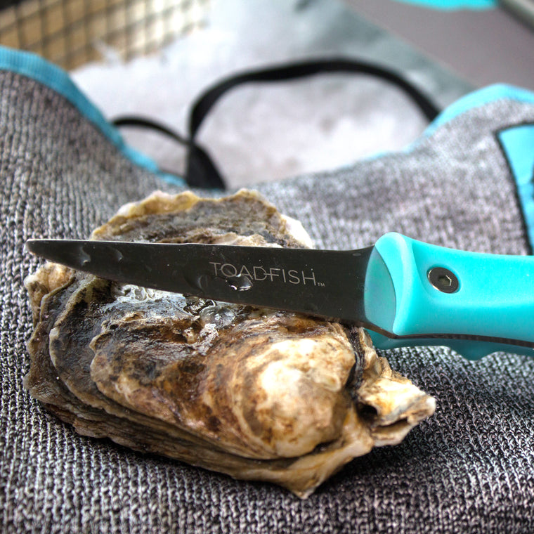 Oyster knife laying on top of whole oyster