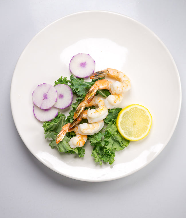 Peeled cooked brown shrimp on kale garnished with lemon slice and radish