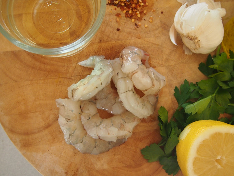 Peeled white shrimp surrounded by lemon, garlic and parsley on wood cutting board 
