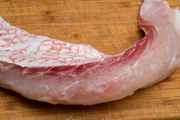 A piece of fresh red snapper on a wooden cutting board.
