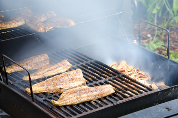 Smoked mullet fish on a grill, being smoked over wood chips with smoke rising. 