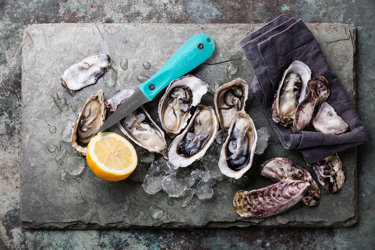 Oysters, oyster knife, tea towel and lemon laying on stone board