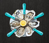 Shucked oysters and oyster knives in star pattern on top of white dish with lemon in the middle thumbnail
