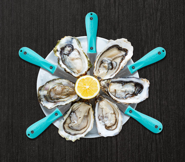 Shucked oysters and oyster knives in star pattern on top of white dish with lemon in the middle