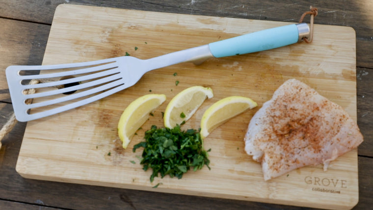 Fish spatula, parsley, lemon slices and fish fillet laying on wood cutting board